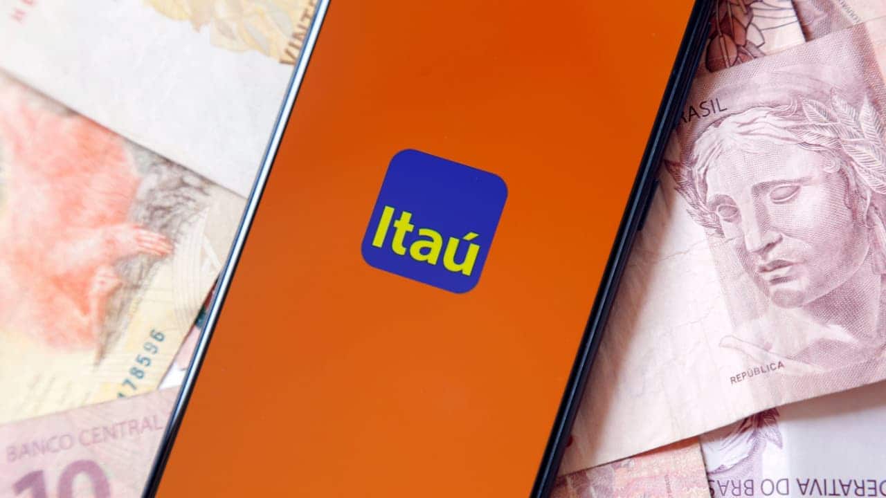 Celular com a logo do ItaĂș na tela em cima de vĂĄrias notas de real. cartĂŁo