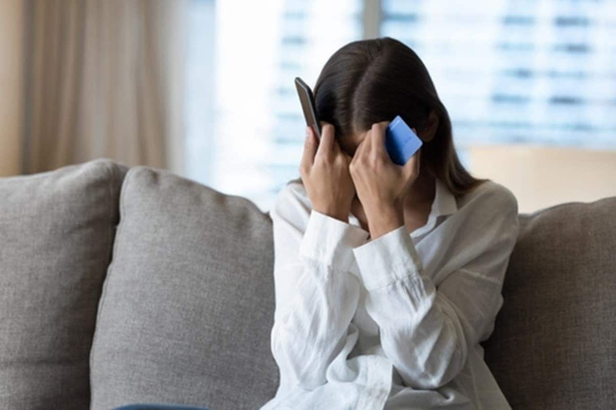 Mulher desesperada com cartão de crétido e celular nas mãos depois de ser vítimas do Golpe da Herança