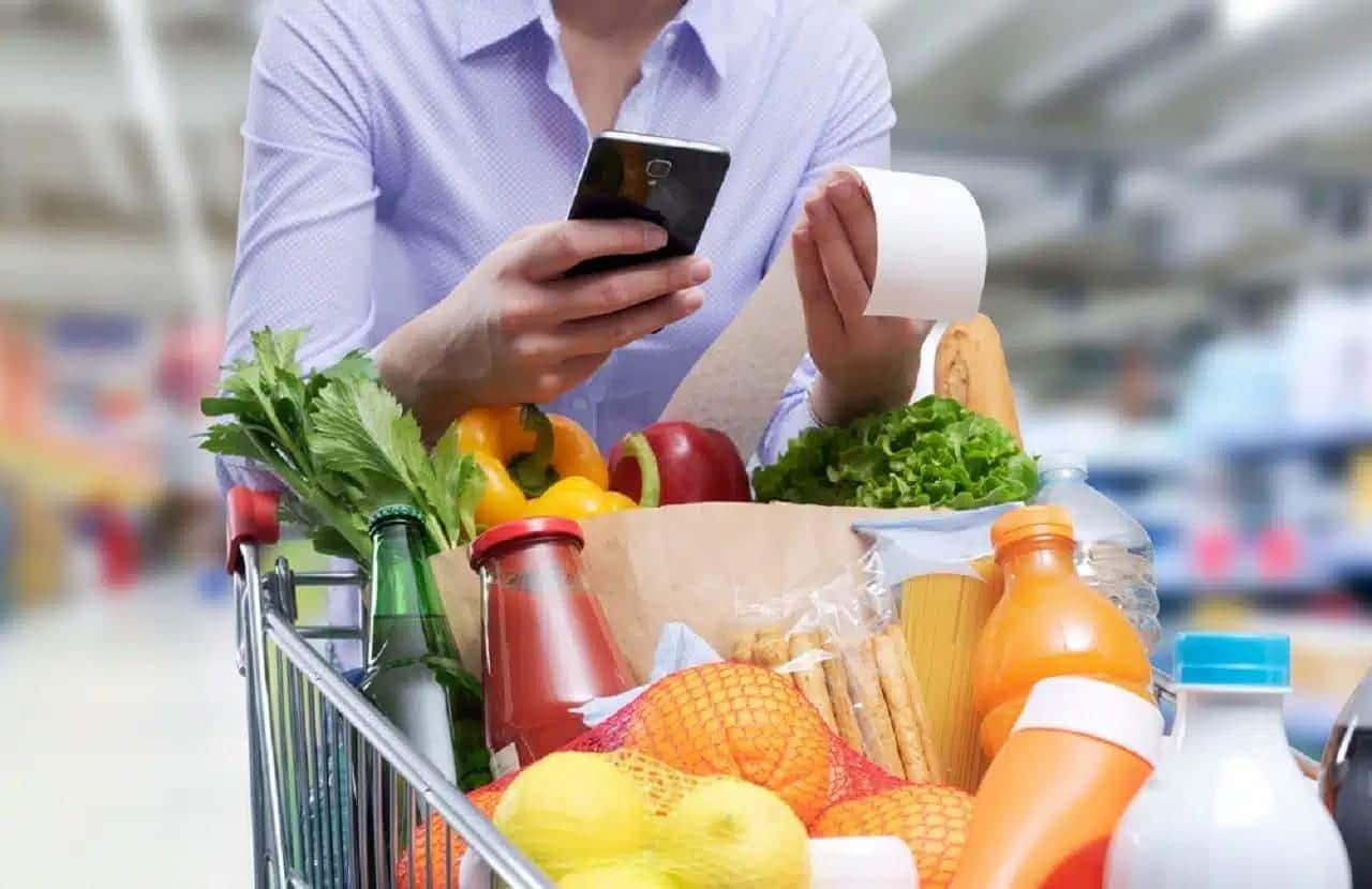 Pessoa com um carrinho de supermercado cheio analisando um extrato. Alimentos dentro do carrinho podem ter sido comprados com o auxílio alimentação