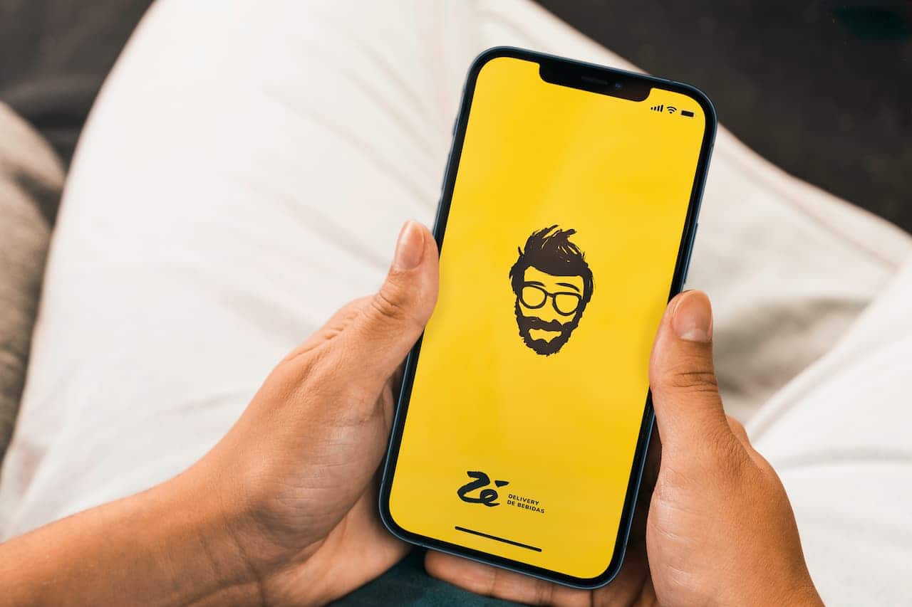 mĂŁos brancas segurando celular com o logo do aplicativo ZĂ© Delivery