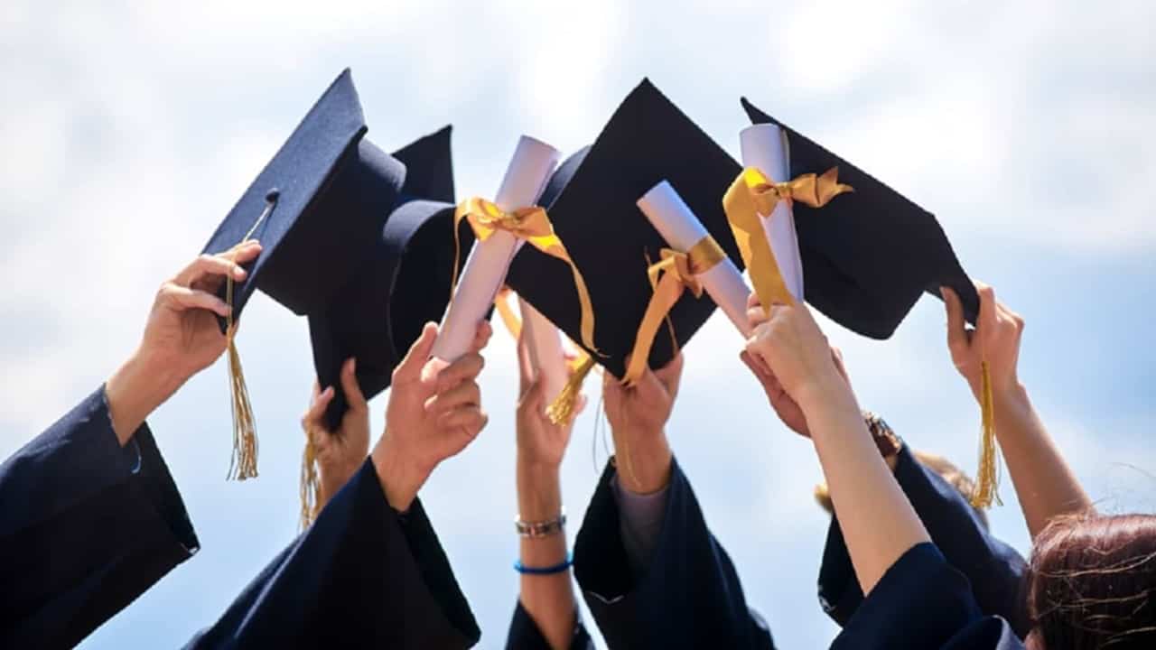 imagens de braços de 7 formandos levantando chapéus e diplomas em uma festa de formatura. Ao fundo, vemos um céu azul com nuvens brancas