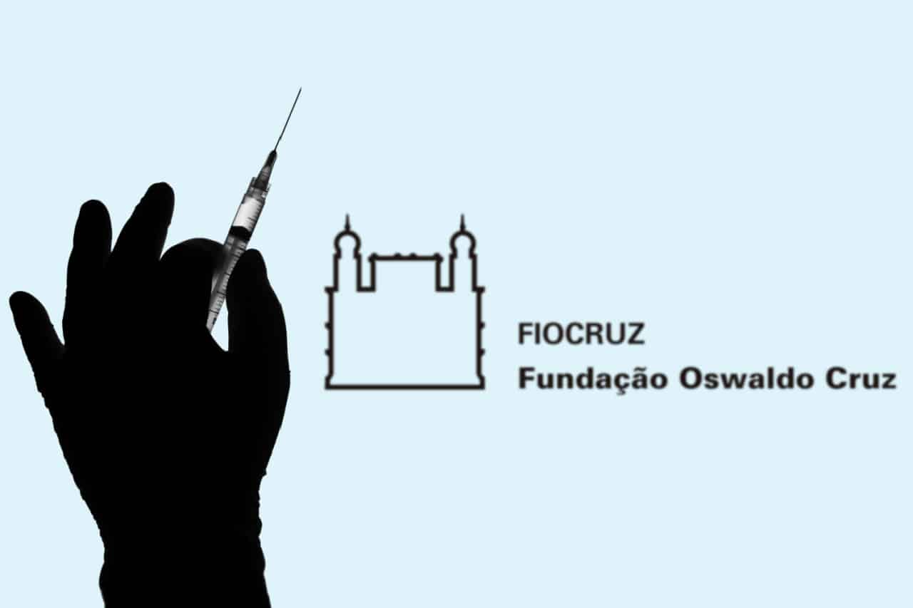 Sombra de uma mão segurando uma seringa com agulha. Ao fundo, logo da Fiocruz (Fundação Oswaldo Cruz).
