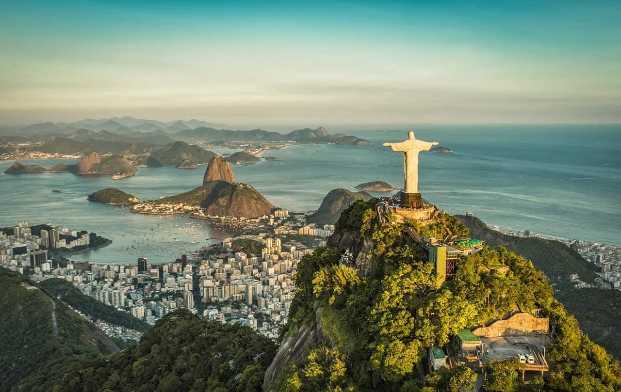 Imagem mostra uma visão aérea do Cristo Redentor, no Rio de Janeiro. Ao fundo, é possível ver um pedaço da cidade e da praia.