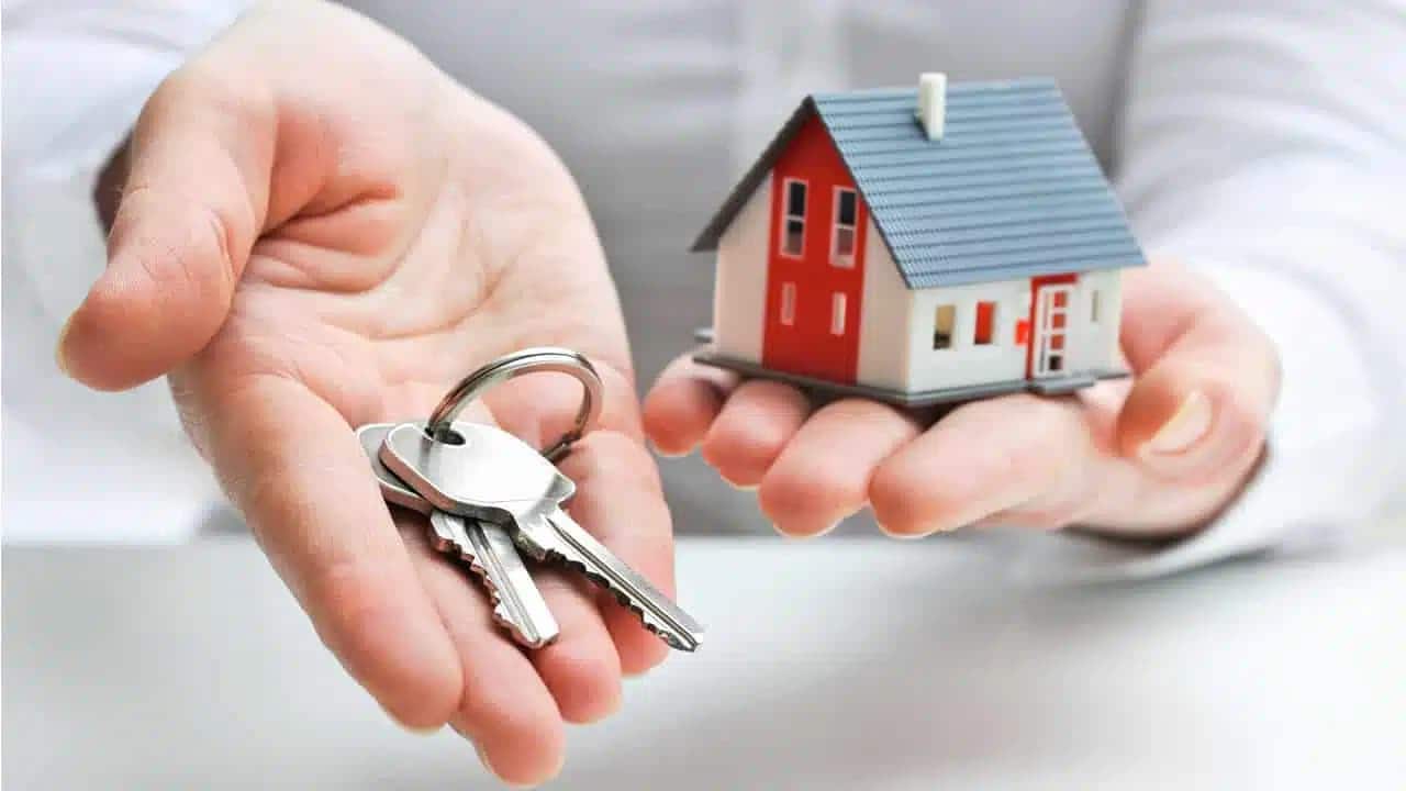 Mãos segurando um molho de chaves e uma miniatura de casa