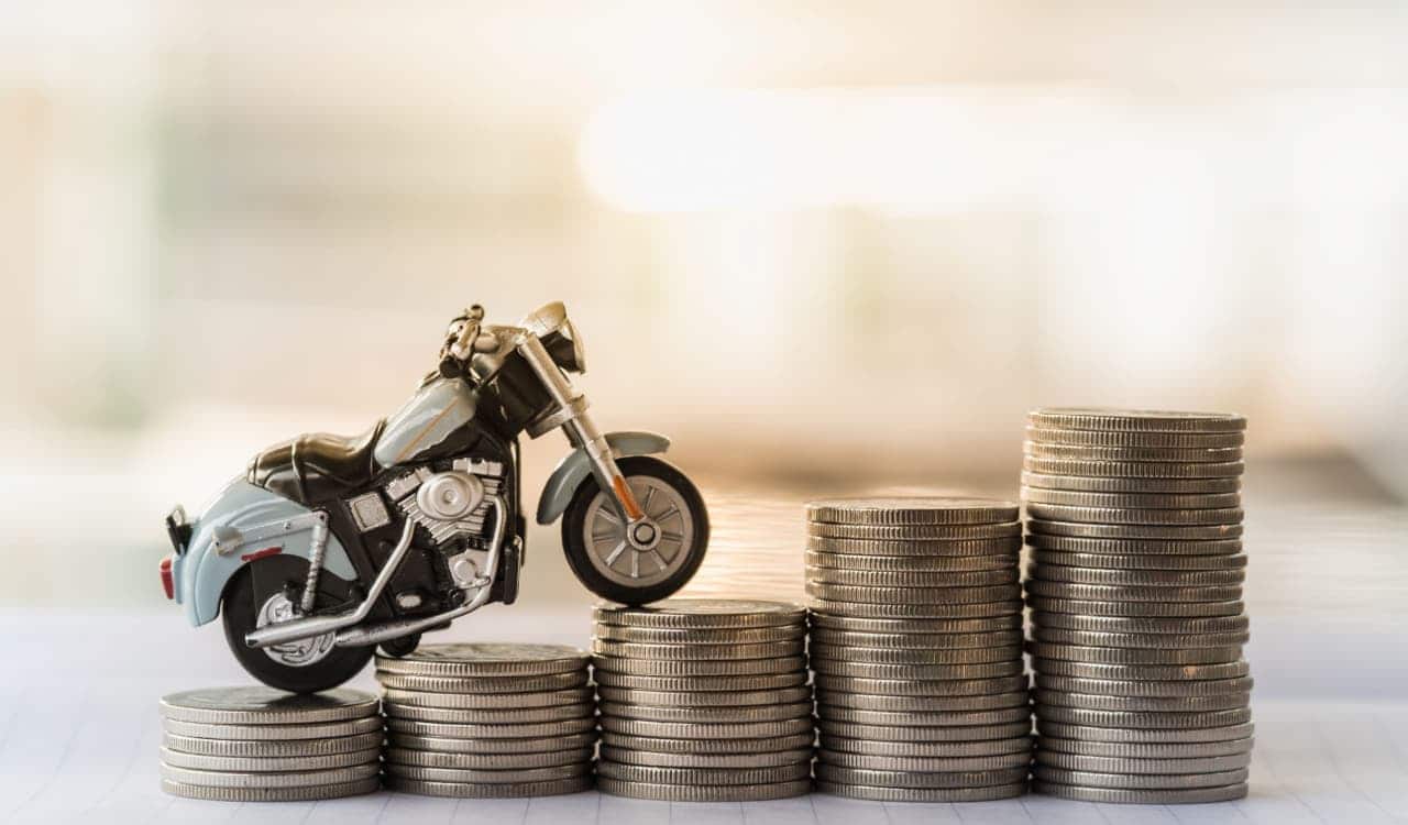 Miniatura de uma moto subindo pilhas de moedas