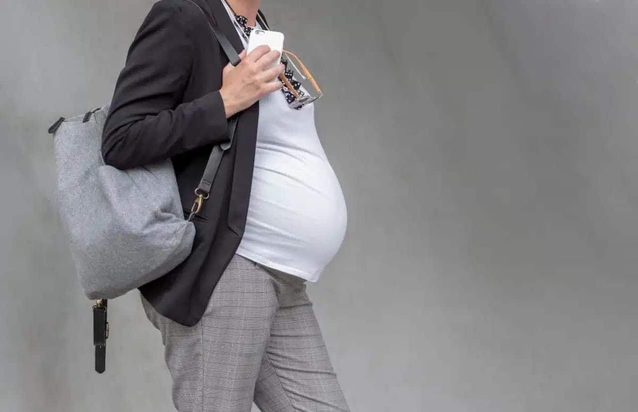 Imagem de uma mulher grávida segurando uma mochila cinza