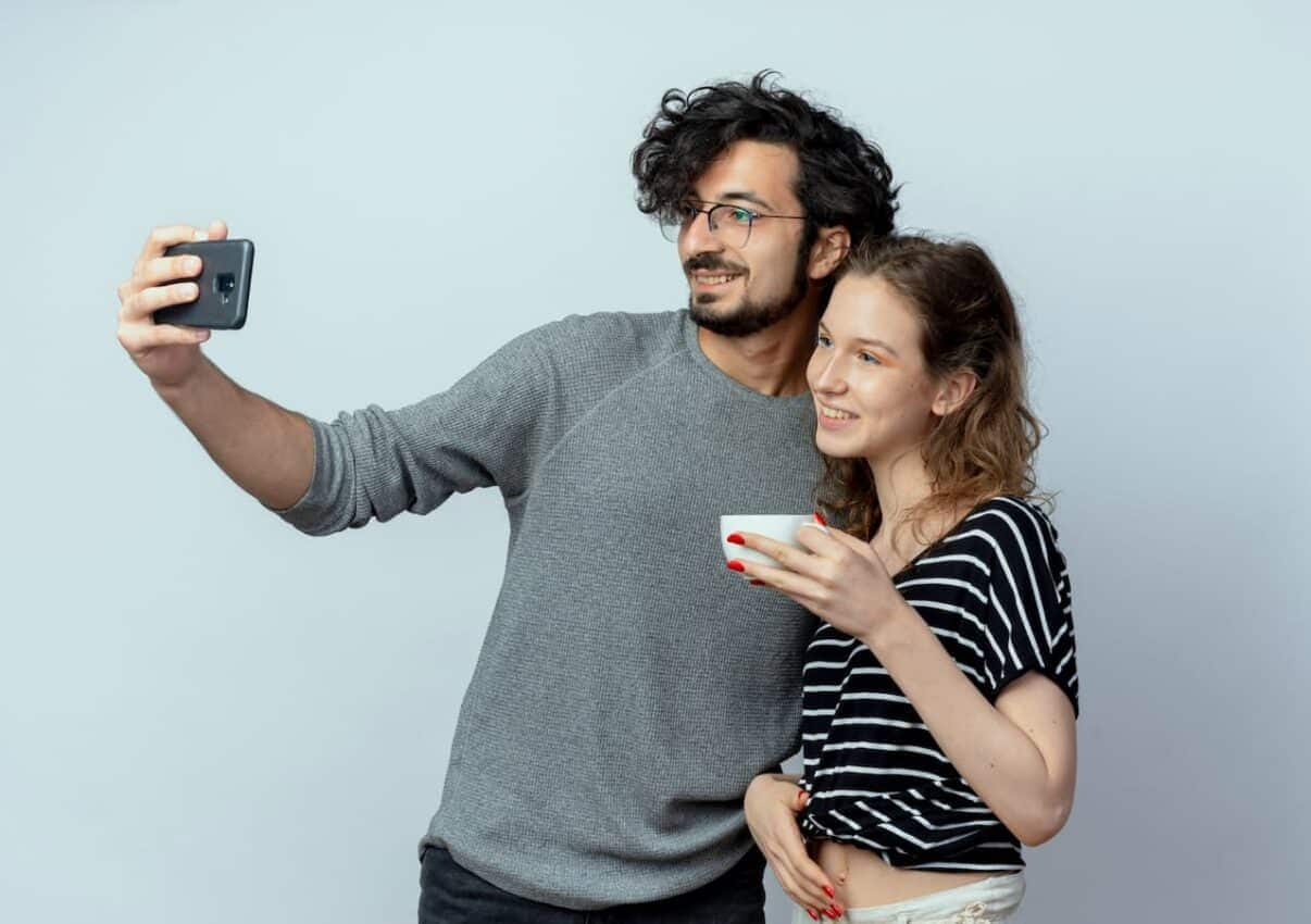 Homem segurando celular enquanto tira foto ao lado de uma mulher