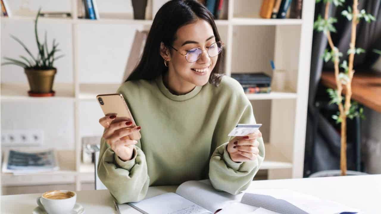 mulher segurando o celular em uma mão e o cartão de crédito na outra
