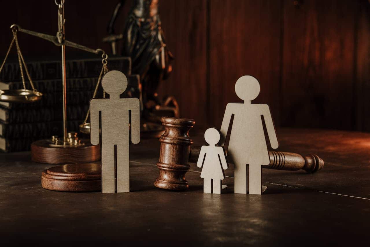 Mesa de escritório com bonecos de madeira que representam membros de uma família, um martelo de tribunal e uma balança da justiça.