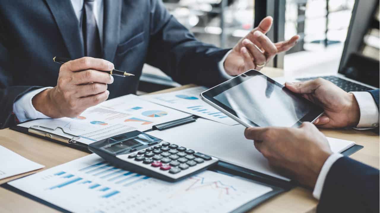 dois investidores conversando sobre negócios enquanto usam um tablet e uma calculadora