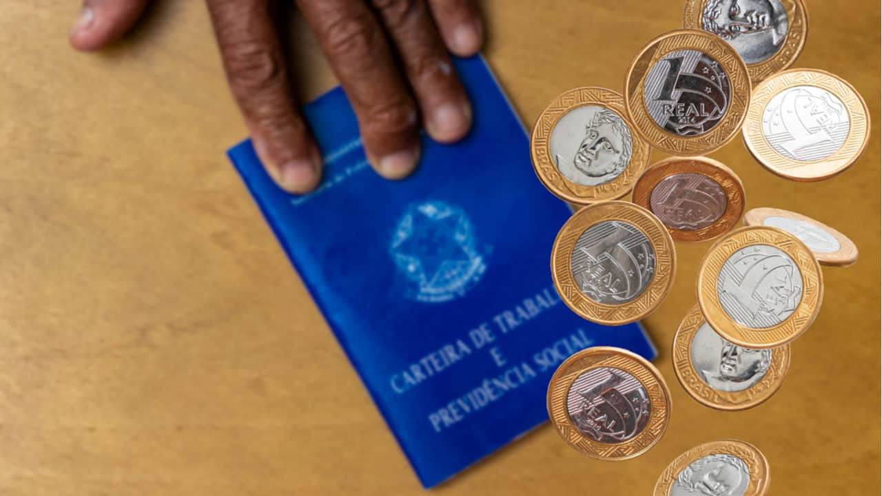 Uma mão sobre uma Carteira de Trabalho e Previdência Social com algumas moedas de um real ao lado