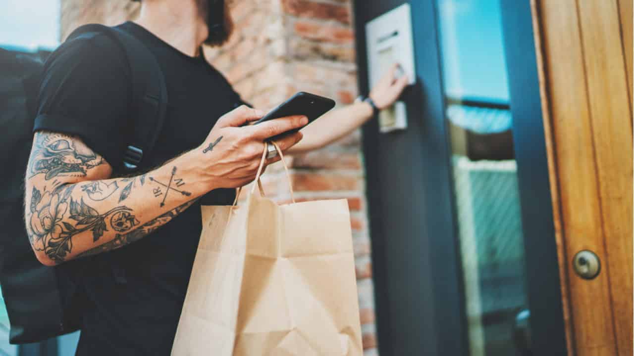 entregador faz entrega de compra delivery em frente a porta enquanto segura celular