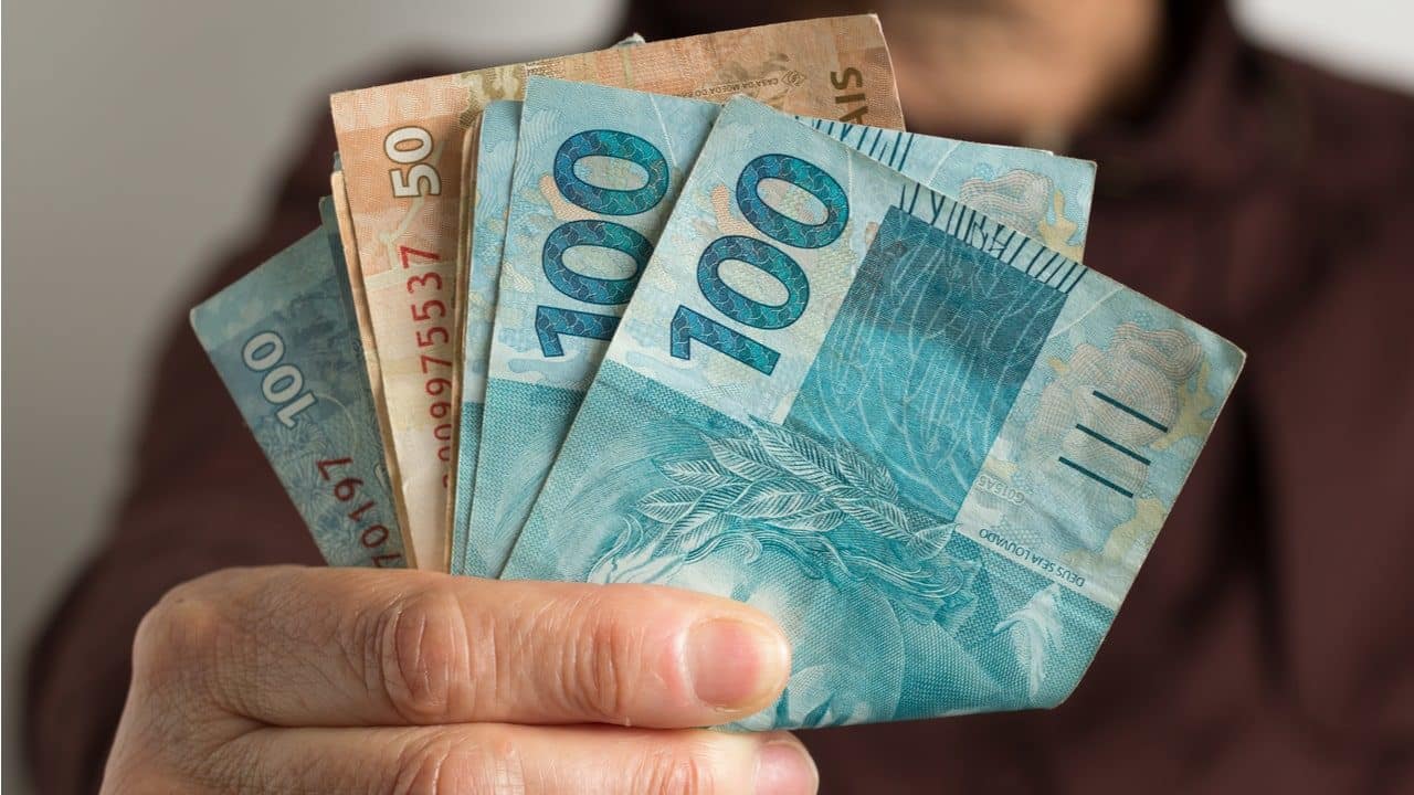 um homem segurando notas de 100 e 50 reais na mão