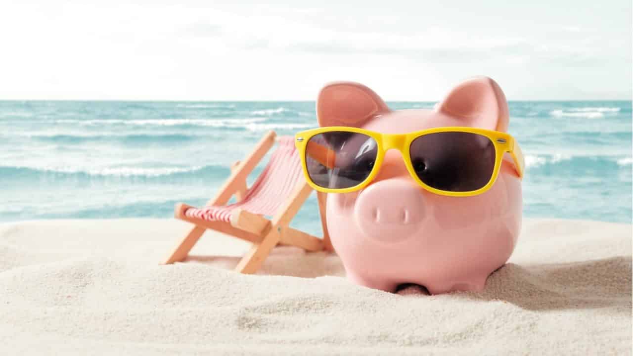 um cofre em formato de porquinho com óculos de sol do lado de uma cadeira na praia