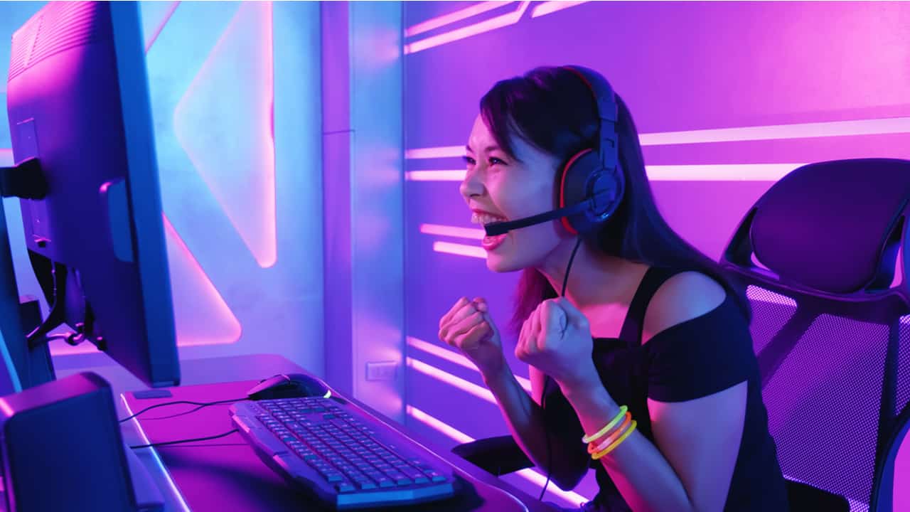 menina se divertindo com jogo, sentada em frente a um computador e usando um headphone