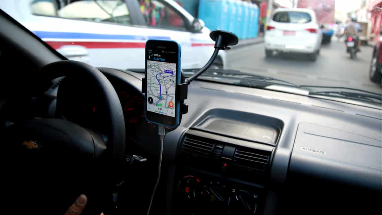 imagem de dentrod e um carro com aplicativo de localização conectado na tela do celular acoplado ao painel do carro