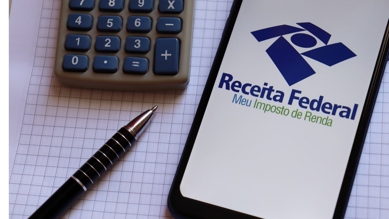 Celular com tela mostrando aplicativo da Receita Federal ao lado de uma caneta e calculadora
