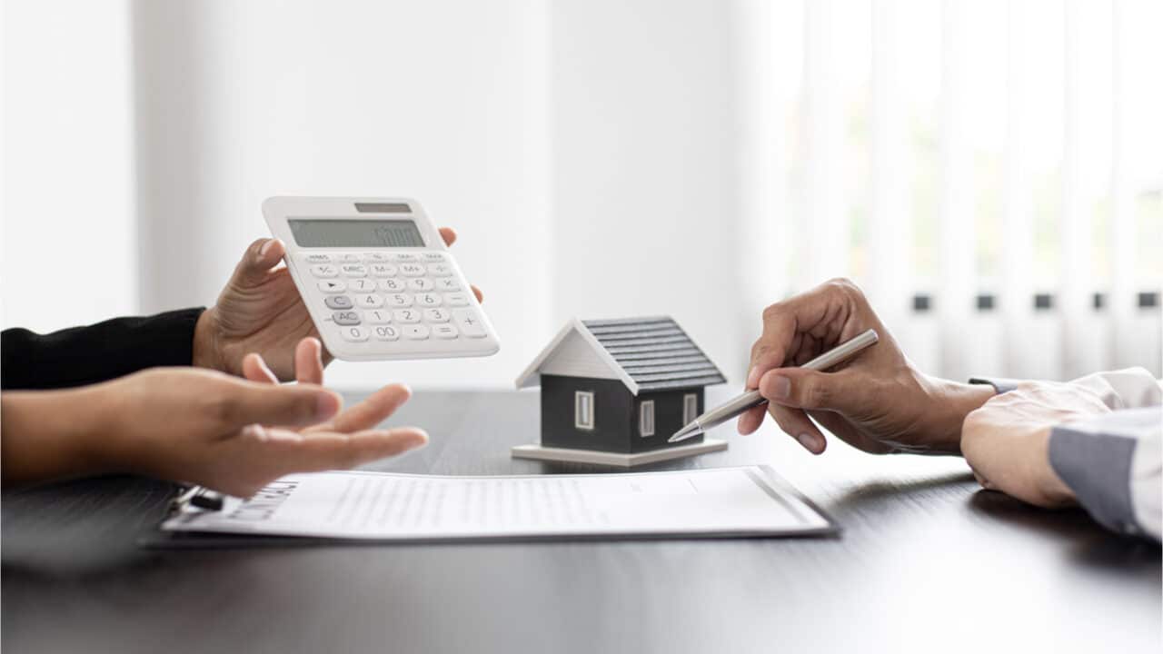 Mesa com documentos e um objeto representando uma casa ao fundo