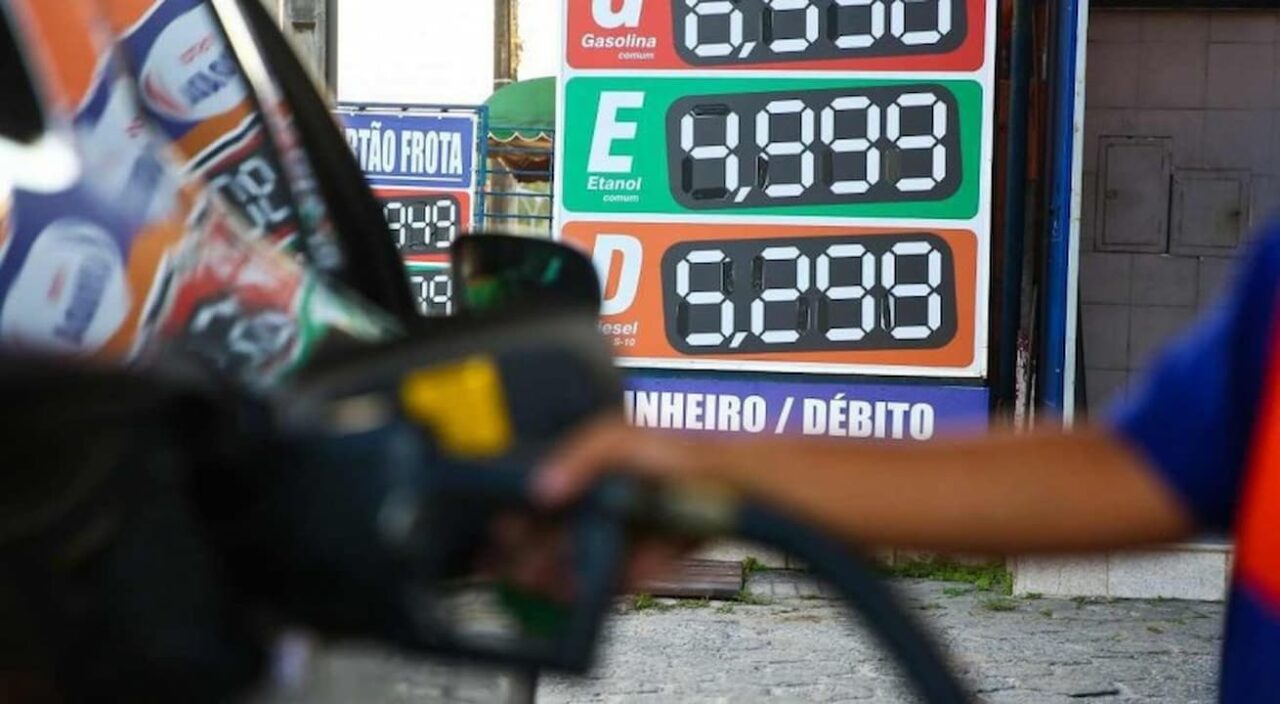 carro sendo abastecido e painel de preços dos combustíveis ao fundo em foco