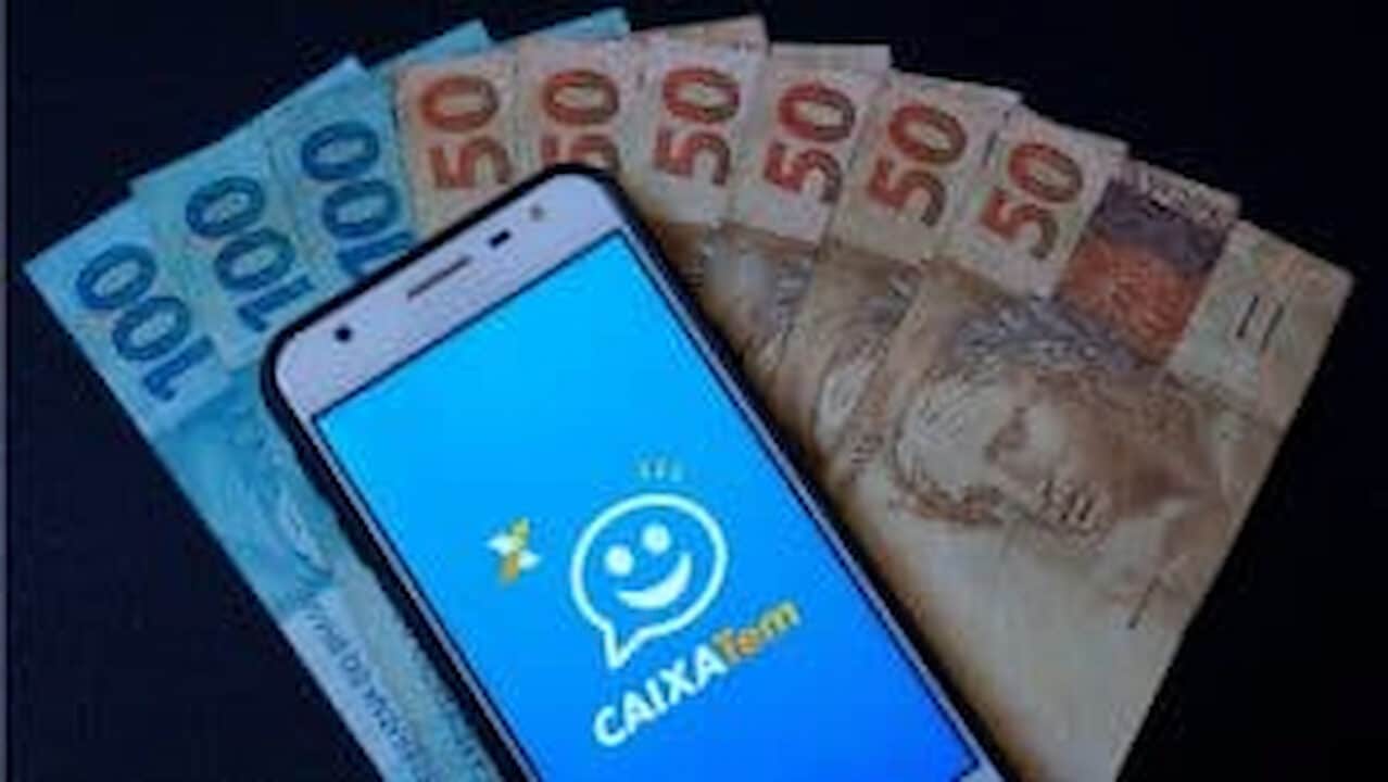 Celular com o aplicativo Caixa Tem na frente de cédulas de real
