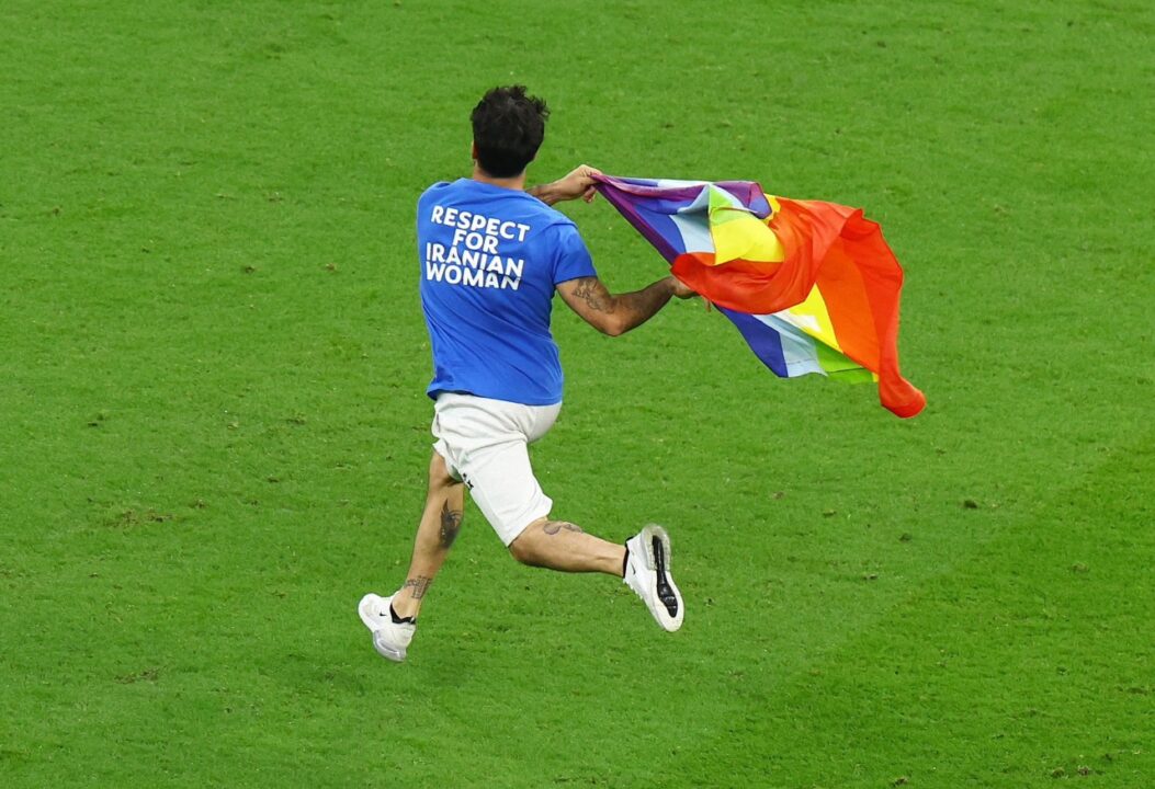 Homem vestido com camiseta azul em defesa às mulheres do Irã segurando bandeira LGBT
