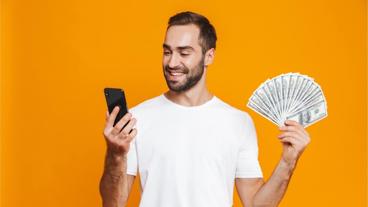 Homem com celular em uma mão e dinheiro extra na outra