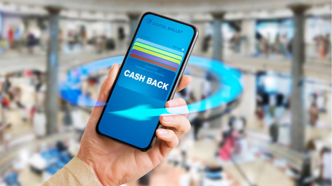 Mão segurando celular que mostra cartões de crédito virtuais e a palavra "cashback"