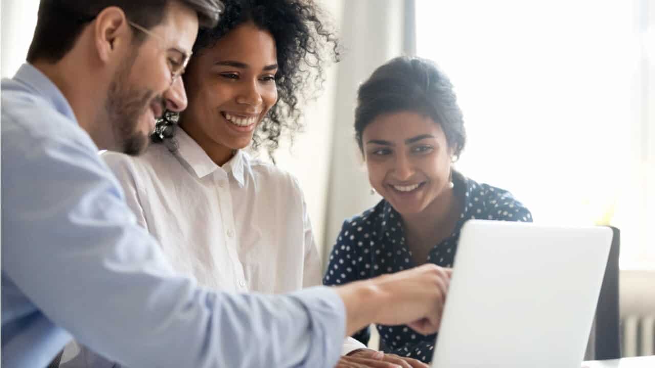 Três pessoas sorrindo olhando para a tela de um notebook