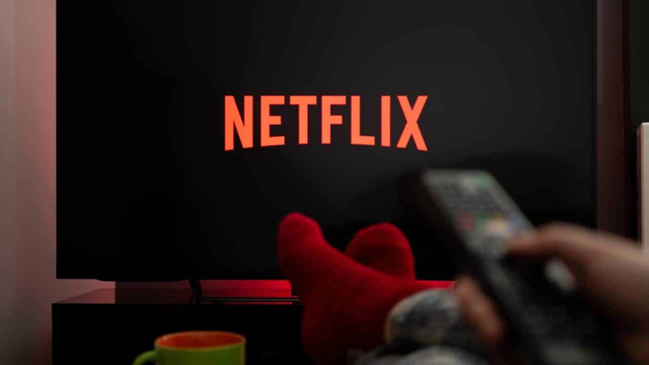 Controle remoto na mão e TV com logo da Netflix