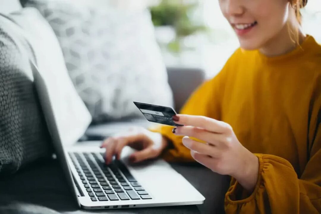 Mulher olhando cartão que segura na mão enquanto digita no computador