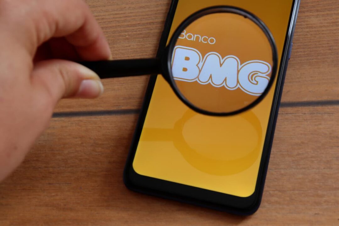 Celular com logo do banco BMG com uma lupa sobre a tela