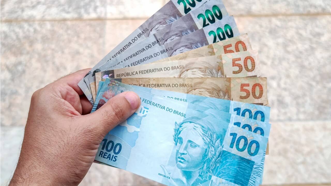 Pessoa segurando notas de 50, 100 e 200 reais