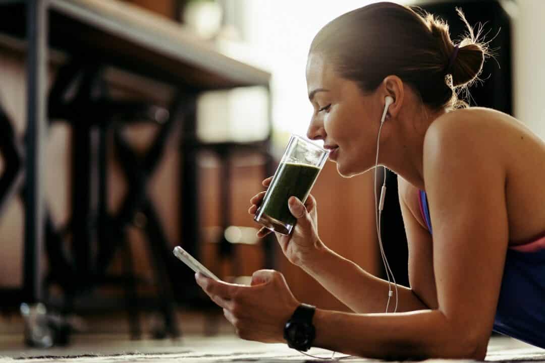 mulher com fones de ouvido tomando suco enquanto olha o celular