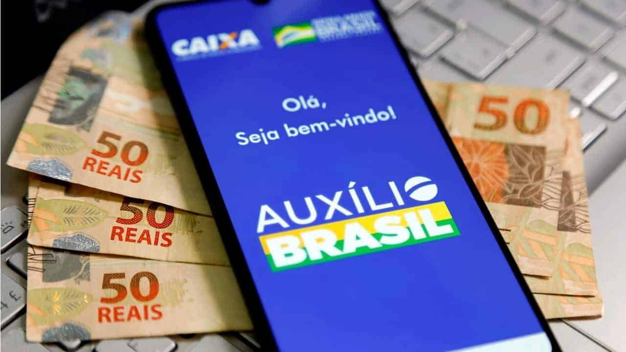 Celular exibindo a tela inicial do aplicativo do Auxílio Brasil em cima de notas de dinheiro