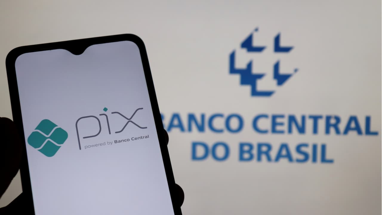 Celular que mostra logo do Pix e logo do Banco Central do Brasil ao fundo
