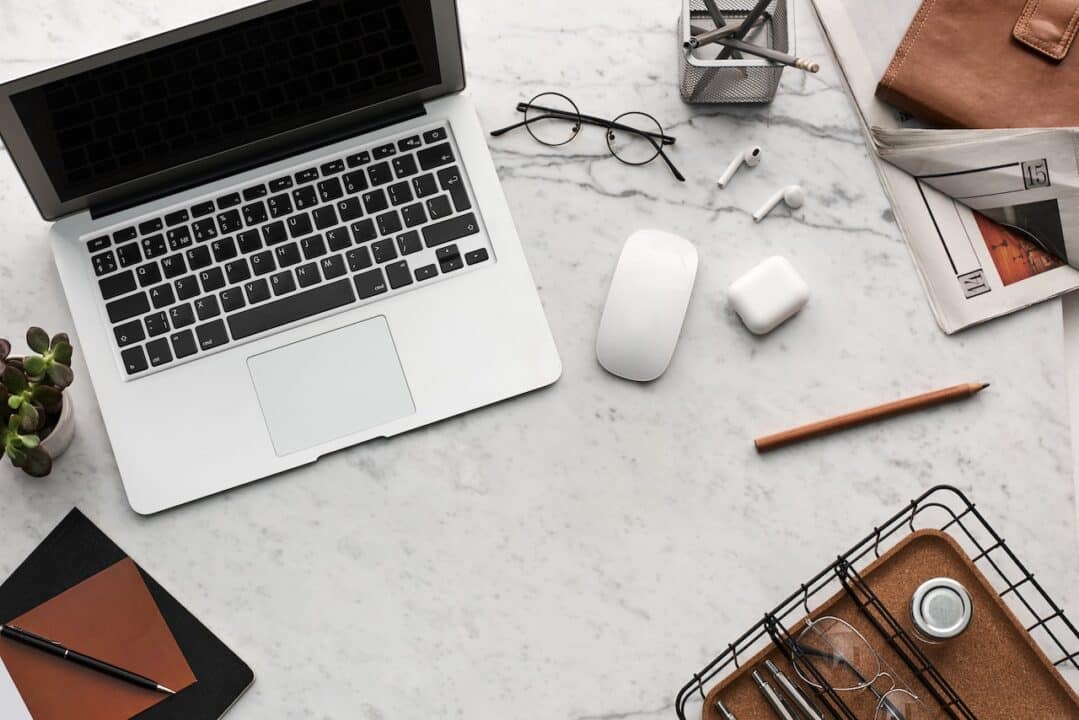Mesa com notebook, mouse, óculos entre outros acessórios.