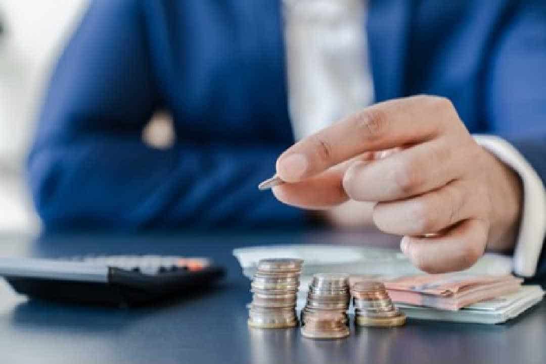 homem contando moedas e notas em cima de uma mesa, na qual tem também uma calculadora