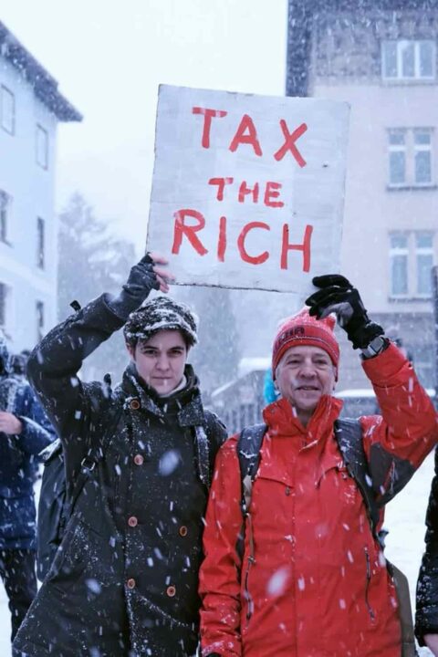 Marlene Engelhorn (esquerda) e Phil White (direita) segurando uma placa que diz "Tax the rich"(taxem os ricos).