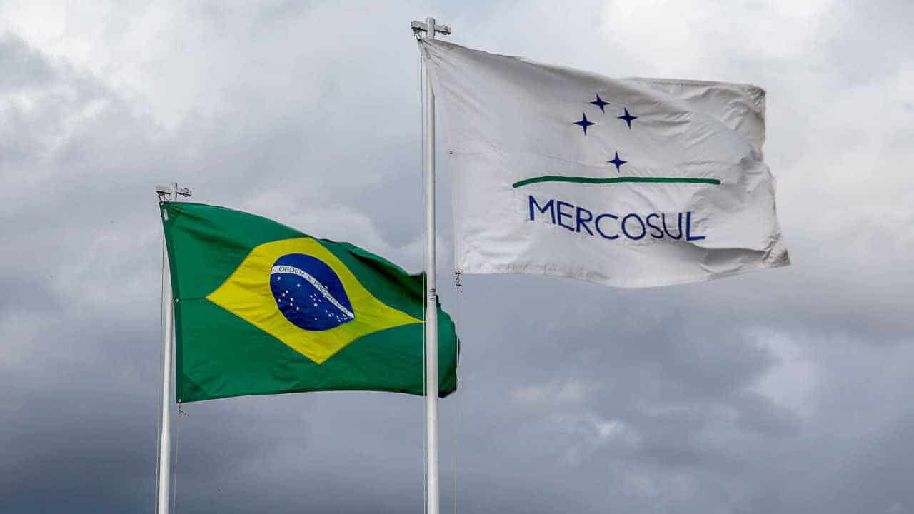 Bandeira do Brasil atrás e à direita e bandeira do Mercosul à frente e à esquerda