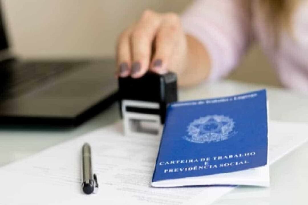 mão feminina carimbando um documento ao lado de uma carteira de trabalho