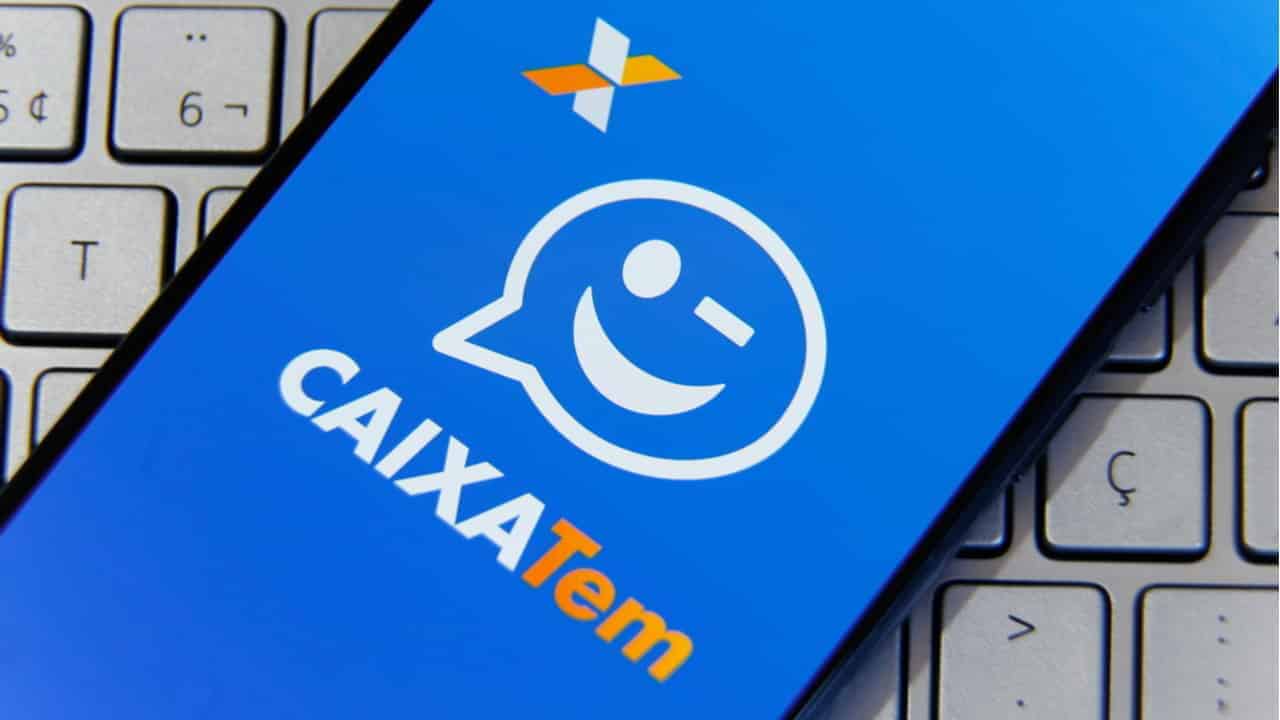 Imagem de um celular com o app do Caixa Tem abertosobreposto em um teclado de notebook