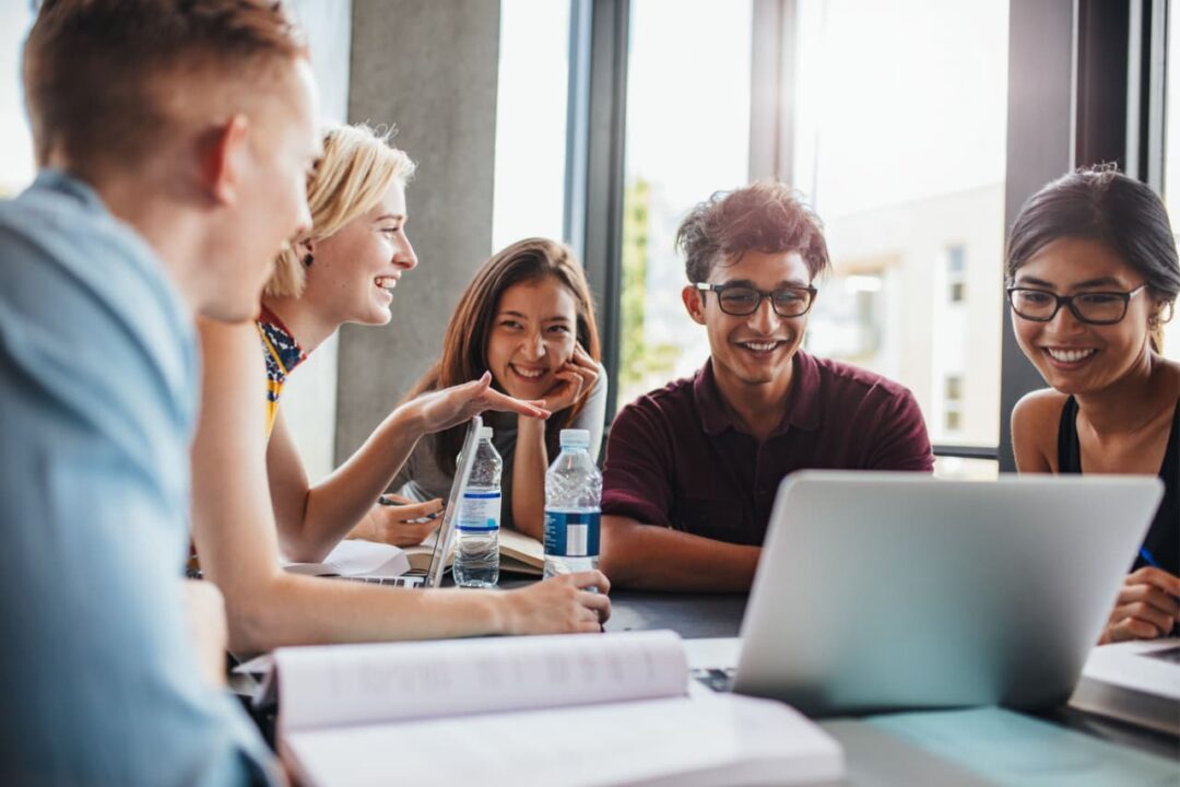 Grupo de jovens sentados à mesa com livros e um notebook aberto