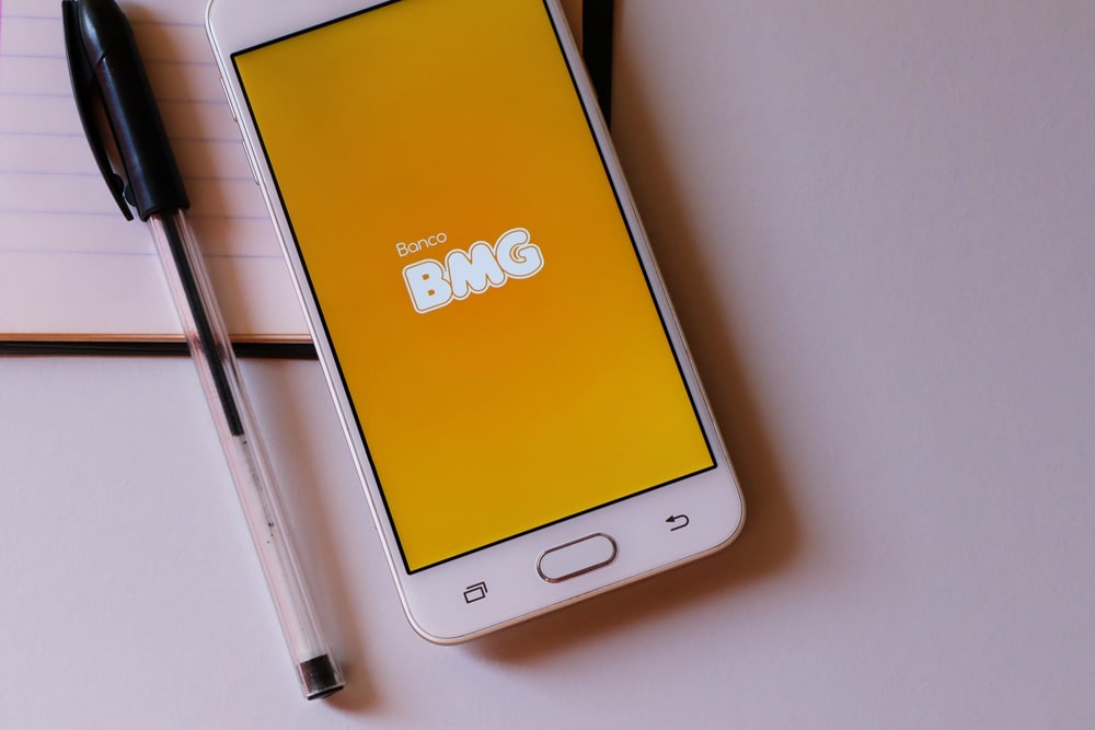 Imagem de um celular com a tela ligada aparecendo o logo do banco BMG.