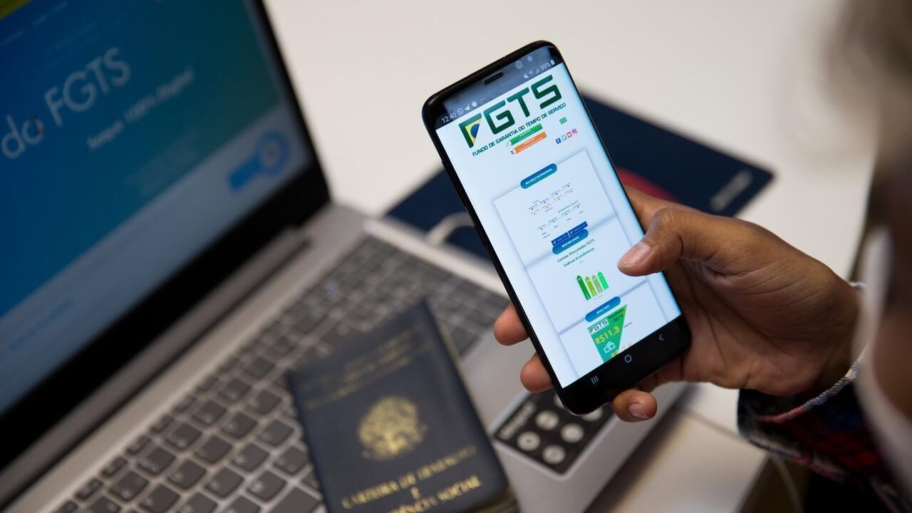 Computador com carteira de trabalho e celular com print do aplicativo FGTS