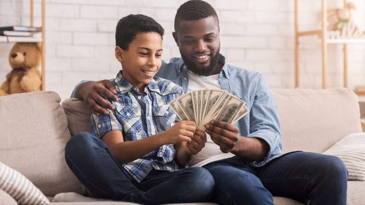 pai e filho sentados no sofá seguram notas de dinheiro sorrindo