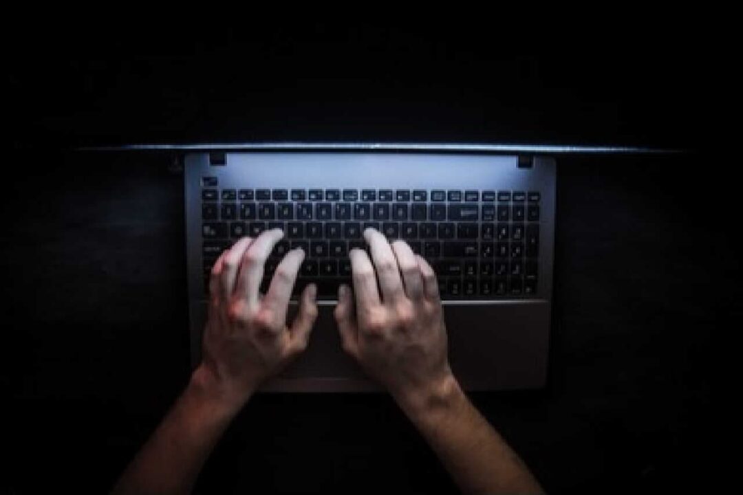 mãos digitam no teclado de um notebook em meio a escuridão