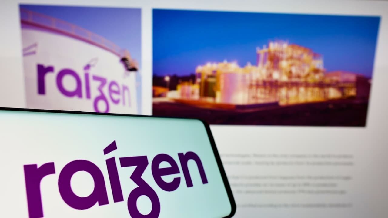 Celular com logotipo da empresa brasileira de energia Raizen S.A. na tela em frente ao seu site comercial.