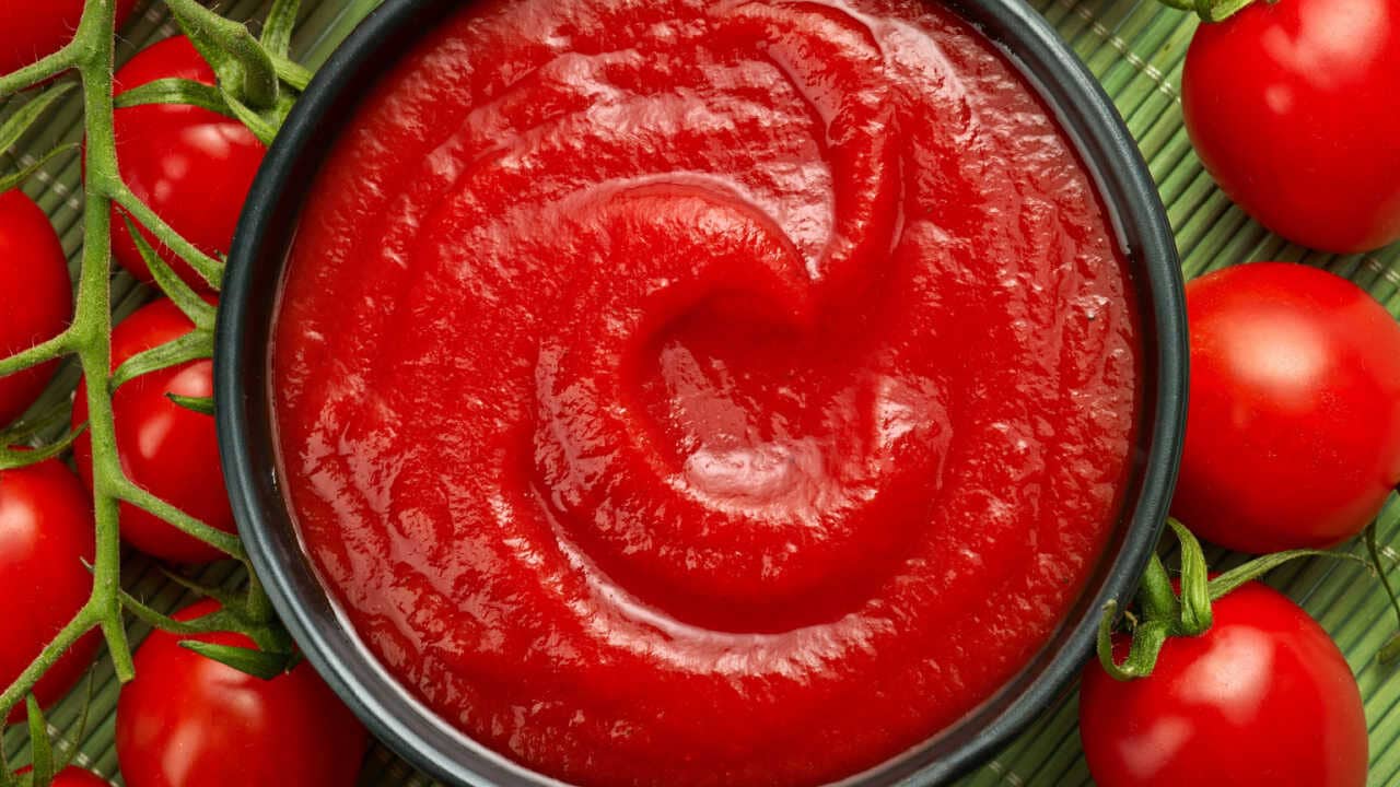 Imagem de molho de tomate em uma tigela e tomates maduros em volta
