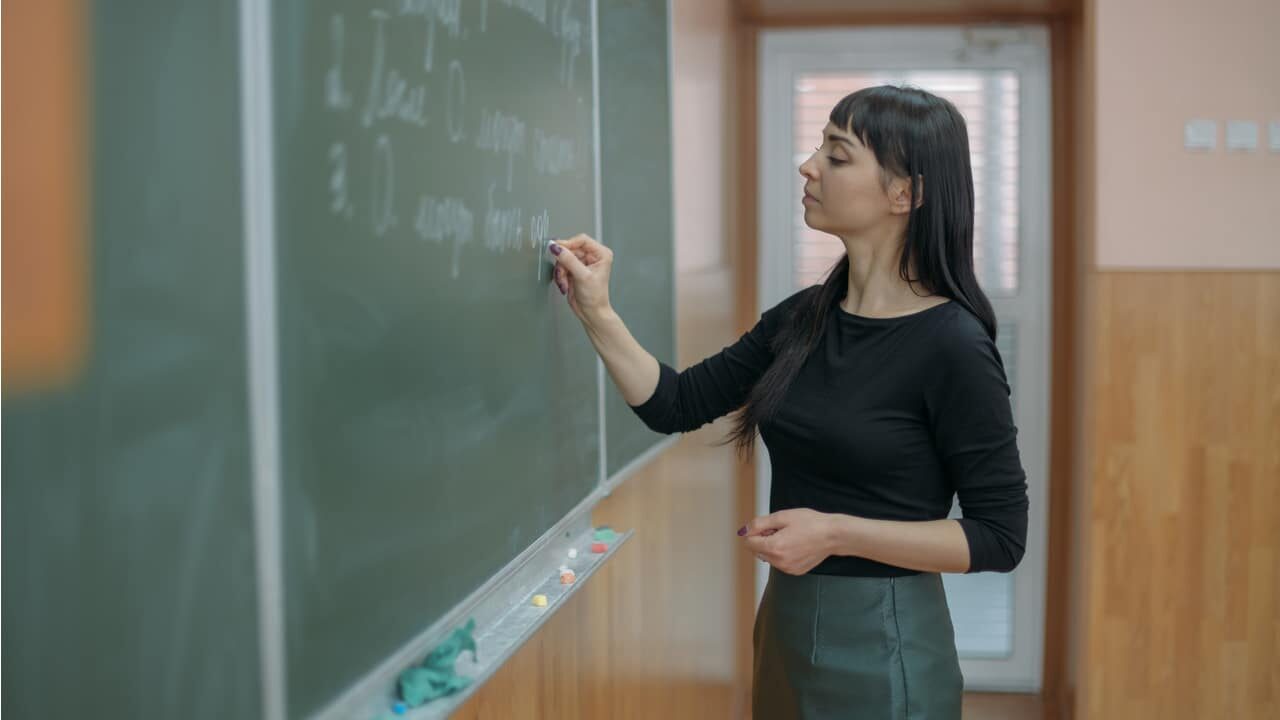 Professora trabalha escrevendo em quadro negro de sala de aula