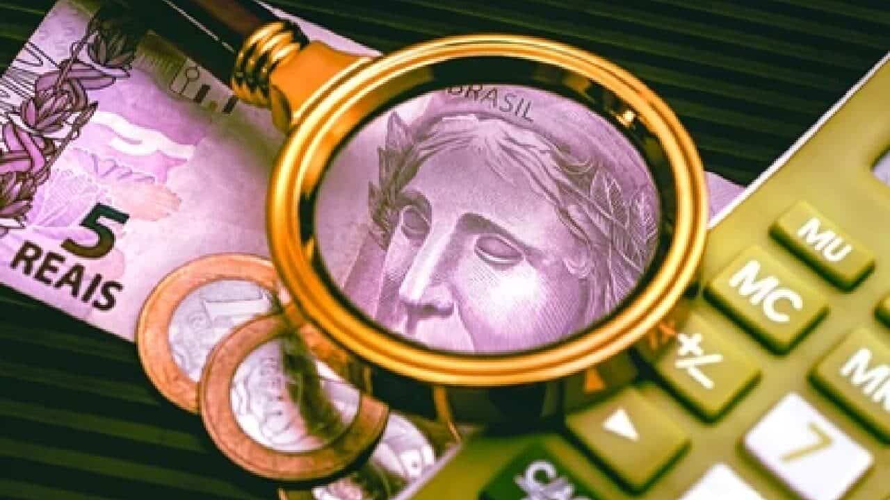 Lupa em cima de notas de real e moedas